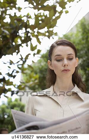 Stock Photo - A Young Adult Businesswoman Reading a Newspaper, Head and Shoulders, Front View, Low Angle View, Differential Focus. Fotosearch