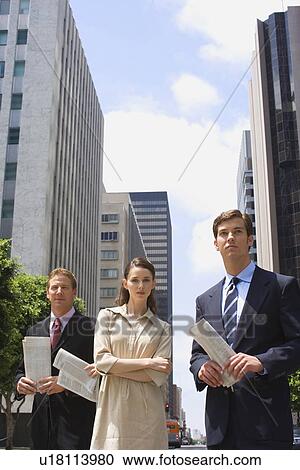 Stock Image - Three Office Workers Standing in the Downtown, Front View, Low Angle View, Three Quarter Length. Fotosearch