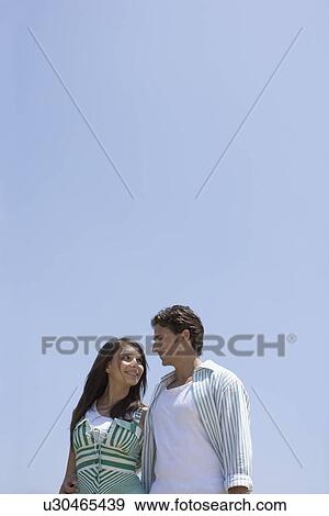 Young adult couple holding and looking at each other, Low Angle View, Copy Space View Large Photo Image Stock Photo - Young adult couple holding and looking at each other, Low Angle View, Copy Space. Fotosearch