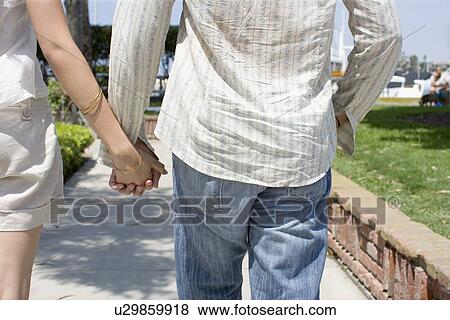 Young adult couple holding hands and walking, Rear View, Differential Focus View Large Photo Image Stock Photo - Young adult couple holding hands and walking, Rear View, Differential Focus. Fotosearch