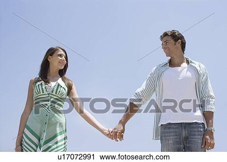 Stock Image - Young adult couple holding hands, Low Angle View. Fotosearch