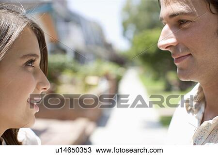 Stock Image - Young adult couple smiling at each other, Side View, Differential Focus. Fotosearch