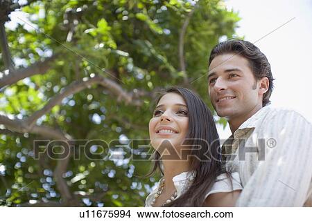 Picture - Young adult couple smiling under a tree, Low Angle View, Differential Focus. Fotosearch