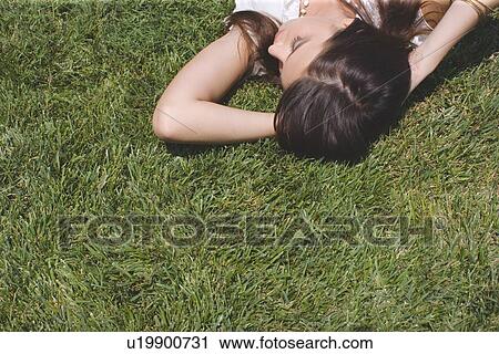 Stock Image - Young adult woman lying down on grass, High Angle View. Fotosearch