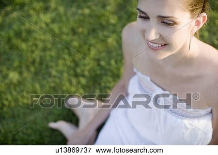 Stock Photo - Young adult woman smiling and sitting on grass, High Angle View, Differential Focus, Copy Space. Fotosearch