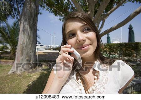 Stock Photo - Young adult woman talking on mobile phone, Front View. Fotosearch