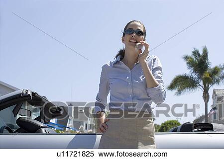 Young adult woman talking on mobile phone by a car, Low Angle View View Large Photo Image Stock Photography - Young adult woman talking on mobile phone by a car, Low Angle View. Fotosearch