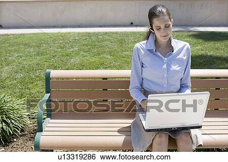 Stock Photograph - Young adult woman using a laptop computer outdoors, High Angle View. Fotosearch