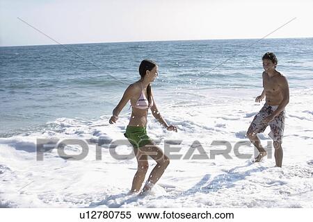 Stock Photography - Young adult couple playing in ocean, Side View. Fotosearch