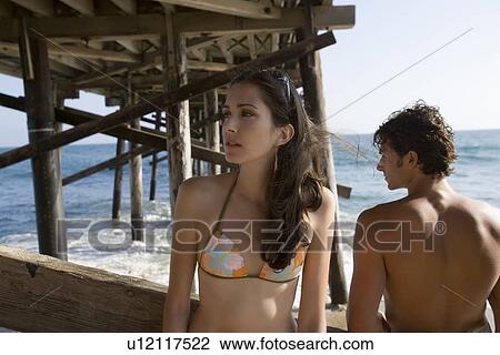 Stock Image - Young adult couple under pier, Front View, Rear View. Fotosearch