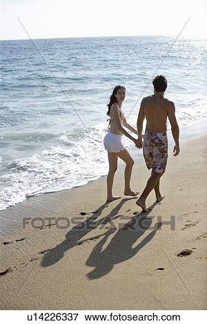 Stock Photo - Young adult couple walking on beach, Side View, Rear View. Fotosearch