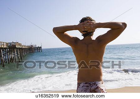 Young adult man looking at the ocean with hands put together behind head, Rear View View Large Photo Image Stock Photo - Young adult man looking at the ocean with hands put together behind head, Rear View. Fotosearch