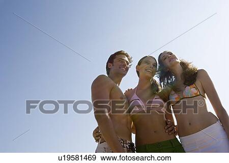Stock Photo - Young adult people smiling on beach, Low Angle View, Lens Flare, Copy Space . Fotosearch