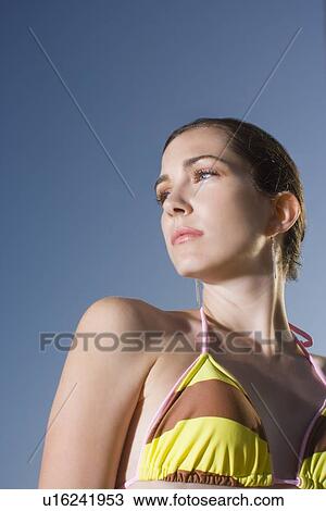 Stock Image - Young adult woman in bikini looking away, Low Angle View. Fotosearch