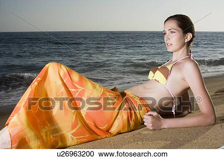 Stock Image - Young adult woman in bikini lying down on beach, Side View. Fotosearch