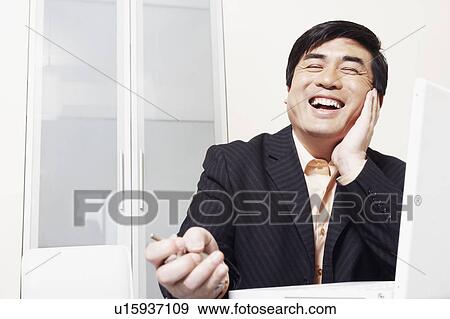 Businessman sitting in front of a laptop laughing View Large Photo Image Stock Photo - Businessman sitting in front of a laptop laughing. Fotosearch