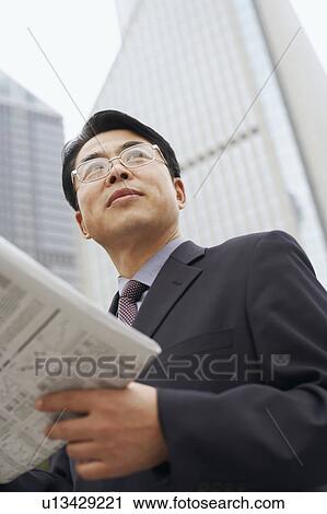 Stock Image - Close-up of a businessman holding a newspaper. Fotosearch