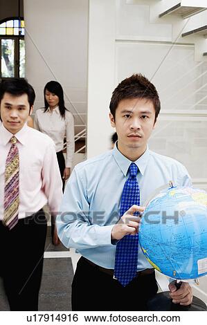 Portrait of a businessman holding a globe with two business executives behind him View Large Photo Image Stock Photograph - Portrait of a businessman holding a globe with two business executives behind him. Fotosearch