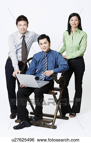 Stock Photograph - Portrait of a businessman holding a laptop with two businesspeople standing beside him. Fotosearch