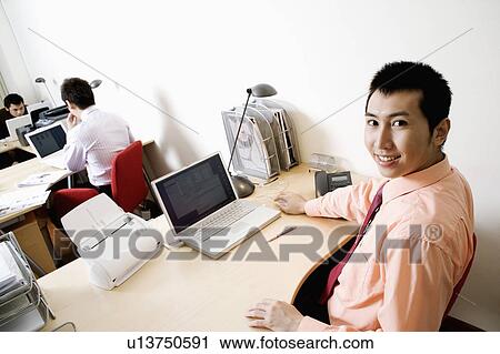 Portrait of a businessman smiling with another businessmen working in the background View Large Photo Image Stock Image - Portrait of a businessman smiling with another businessmen working in the background. Fotosearch