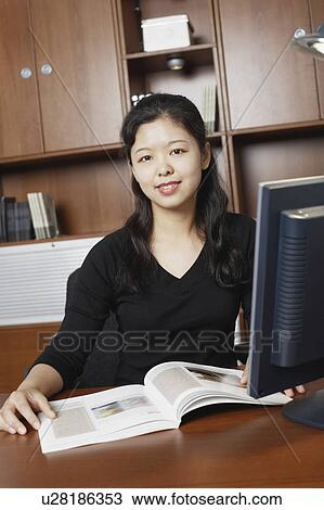 Stock Image - Portrait of a businesswoman sitting with a magazine on the table. Fotosearch