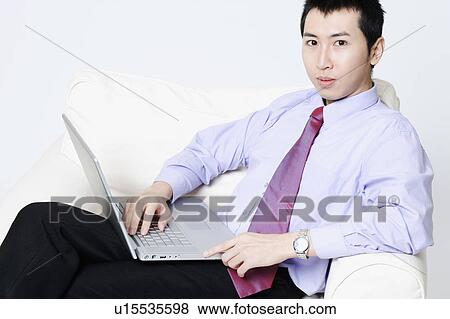 Stock Photo - Portrait of a young businessman sitting in an armchair and using a laptop. Fotosearch