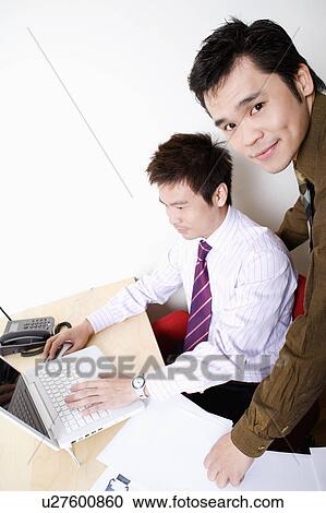 Side profile of a businessman using a laptop with another businessman smiling View Large Photo Image Stock Image - Side profile of a businessman using a laptop with another businessman smiling. Fotosearch