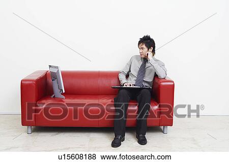 Stock Photo - Businessman sitting on a couch and looking at computer monitor. Fotosearch