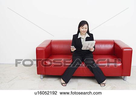 Businesswoman sitting on a couch holding a newspaper and a mobile phone View Large Photo Image Stock Image - Businesswoman sitting on a couch holding a newspaper and a mobile phone. Fotosearch
