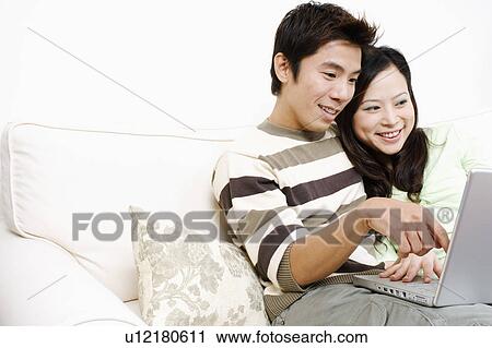 Close-up of a mid adult man sitting on a couch with a young woman using a laptop View Large Photo Image Stock Image - Close-up of a mid adult man sitting on a couch with a young woman using a laptop. Fotosearch