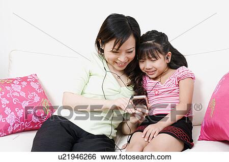 Close-up of a young woman and her daughter listening to an MP3 player View Large Photo Image Stock Photograph - Close-up of a young woman and her daughter listening to an MP3 player. Fotosearch