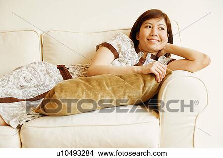 Picture - Close-up of a young woman lying on a couch and smiling. Fotosearch