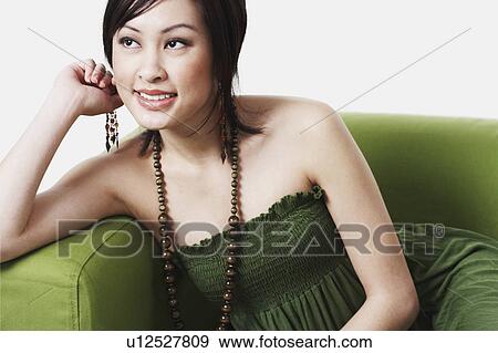 Close-up of a young woman sitting on a couch smiling View Large Photo Image Stock Photo - Close-up of a young woman sitting on a couch smiling. Fotosearch