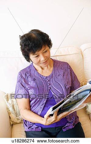 Mature woman sitting on a couch and reading a magazine View Large Photo Image Picture - Mature woman sitting on a couch and reading a magazine. Fotosearch
