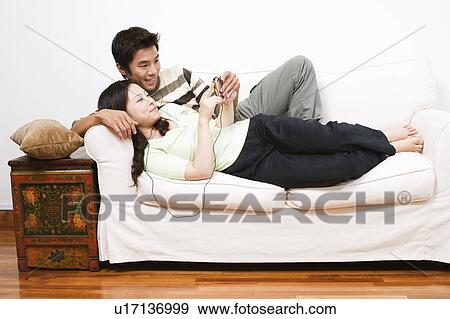 Mid adult man and a young woman lying on a couch and listening to an MP3 player View Large Photo Image Stock Photo - Mid adult man and a young woman lying on a couch and listening to an MP3 player. Fotosearch