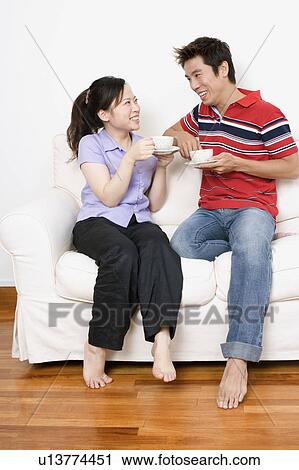 Mid adult man and a young woman sitting on a couch and holding cups View Large Photo Image Stock Image - Mid adult man and a young woman sitting on a couch and holding cups. Fotosearch