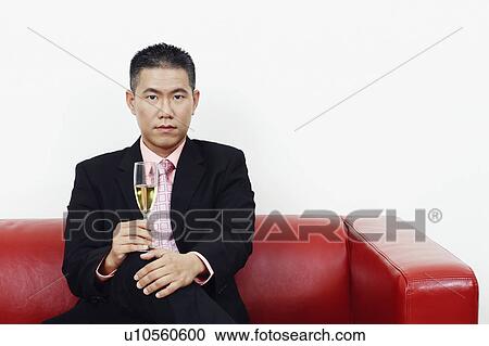 Stock Image - Portrait of a businessman sitting on a couch and holding a champagne flute. Fotosearch