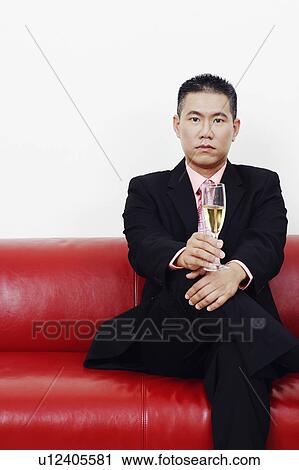 Portrait of a businessman sitting on a couch and holding a champagne flute View Large Photo Image Stock Image - Portrait of a businessman sitting on a couch and holding a champagne flute. Fotosearch
