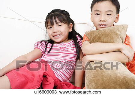 Stock Image - Portrait of a girl sitting on a couch with her brother. Fotosearch
