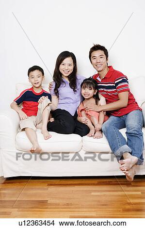 Portrait of a mid adult man and a young woman sitting on a couch with their son and daughter View Large Photo Image Picture - Portrait of a mid adult man and a young woman sitting on a couch with their son and daughter. Fotosearch