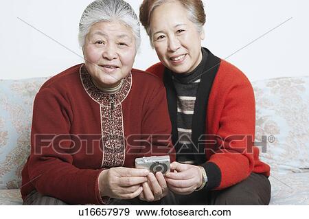 Portrait of a senior woman sitting on a couch with a mature woman holding a digital camera View Large Photo Image Stock Photo - Portrait of a senior woman sitting on a couch with a mature woman holding a digital camera. Fotosearch