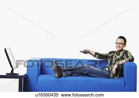 Stock Photography - Portrait of a young man sitting on a couch in front of a flat screen monitor. Fotosearch