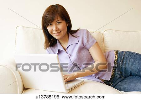 Portrait of a young woman lying on a couch and working on a laptop View Large Photo Image Stock Photograph - Portrait of a young woman lying on a couch and working on a laptop. Fotosearch