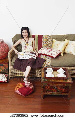 Portrait of a young woman sitting on a couch and holding a magazine View Large Photo Image Stock Image - Portrait of a young woman sitting on a couch and holding a magazine. Fotosearch