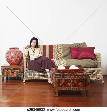 Stock Image - Portrait of a young woman sitting on a couch. Fotosearch