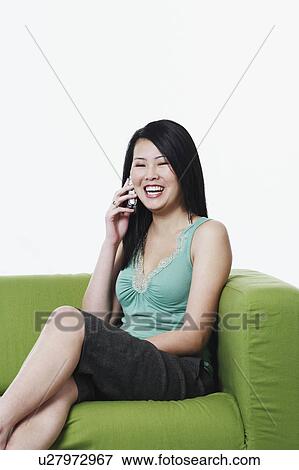 Stock Photo - Portrait of a young woman sitting on a couch talking on a mobile phone. Fotosearch