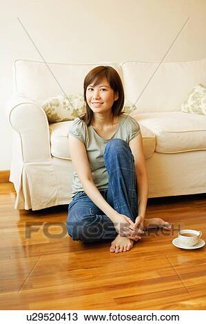 Stock Image - Portrait of a young woman sitting on the floor with a cup of tea beside her. Fotosearch