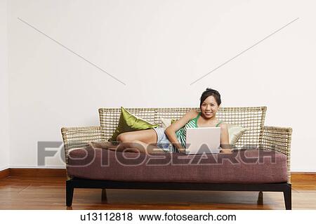 Portrait of a young woman using a laptop on a couch and smiling View Large Photo Image Stock Photo - Portrait of a young woman using a laptop on a couch and smiling. Fotosearch