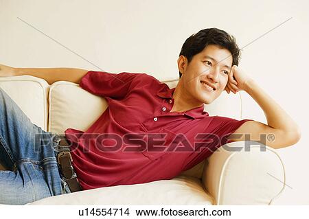 Picture - Young man lying on a couch and smiling. Fotosearch