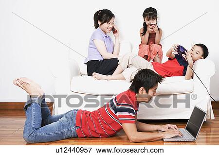 Young woman and her son and daughter sitting on a couch with a mid adult man lying on the floor with a laptop View Large Photo Image Stock Photo - Young woman and her son and daughter sitting on a couch with a mid adult man lying on the floor with a laptop. Fotosearch